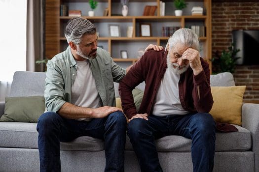 Two men sitting on a couch one is holding his arm up to the other