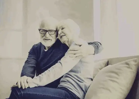 An older couple sitting on a couch hugging.